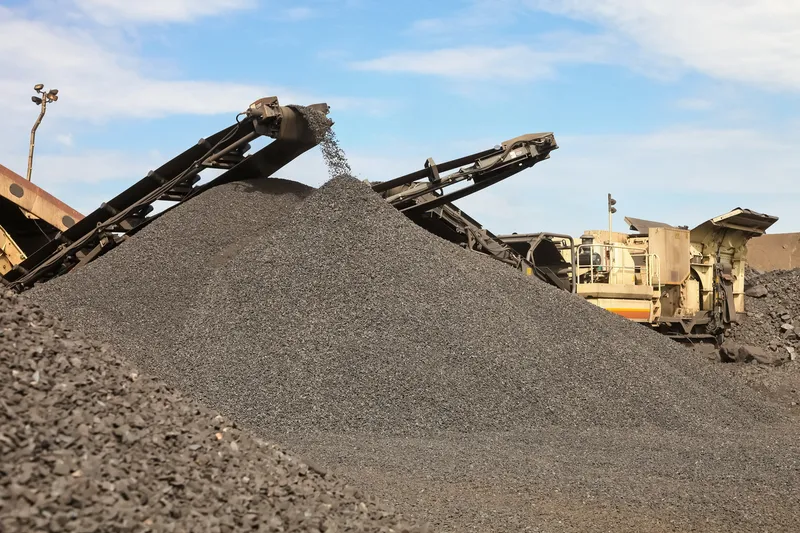 A conveyor dropping crushed stone onto a stockpile under a blue sky